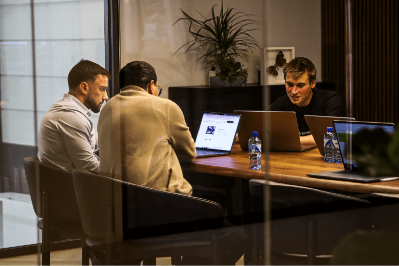 Teamoverleg in de vergaderruimte van SimplyUsed, met medewerkers die samenwerken achter laptops in een moderne kantooromgeving